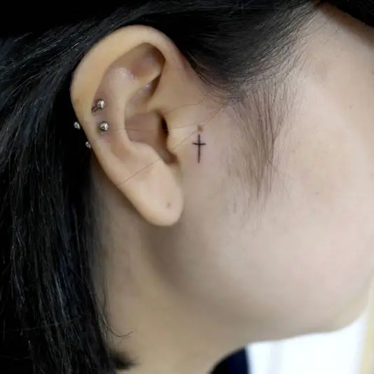 Tiny Black Cross Tattoo Near The Ear