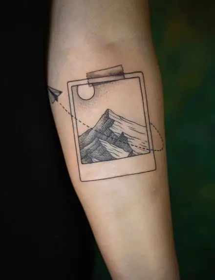 Polaroid Photo with Mountains and Paper Plane Forearm Tattoo