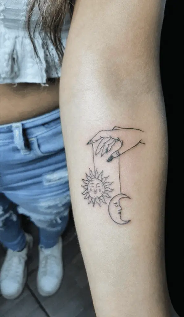 A Hand Grasping Sun and Moon Attached to a Strings Arm Tattoo